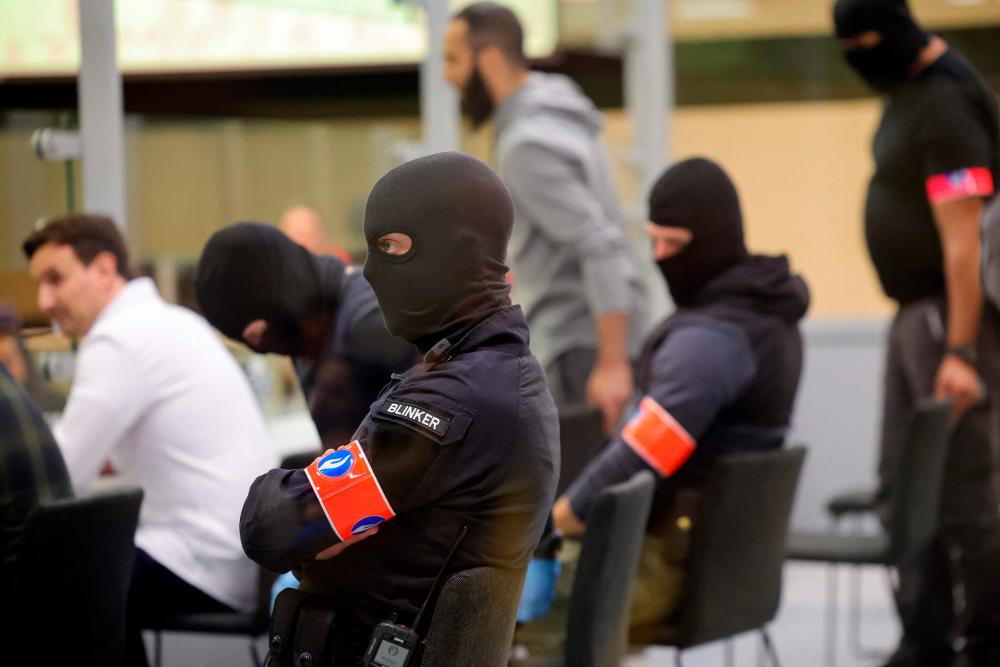 Security personnel oversee defendants as they sit in a specially designed glass box in the courtroom as an unseen judge announces the verdict in the Brussels terrorist attack trial in the Palace of Justice building in Brussels on July 25, 2023. AFPPIX