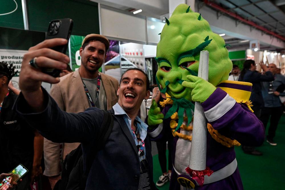A visitor takes a selfie picture with a person in a costume of a cola of a cannabis plant during the Cannabis Expo Brazil, a hemp and cannabis industry exhibition, in Sao Paulo, Brazil, on September 15, 2023. AFPPIX