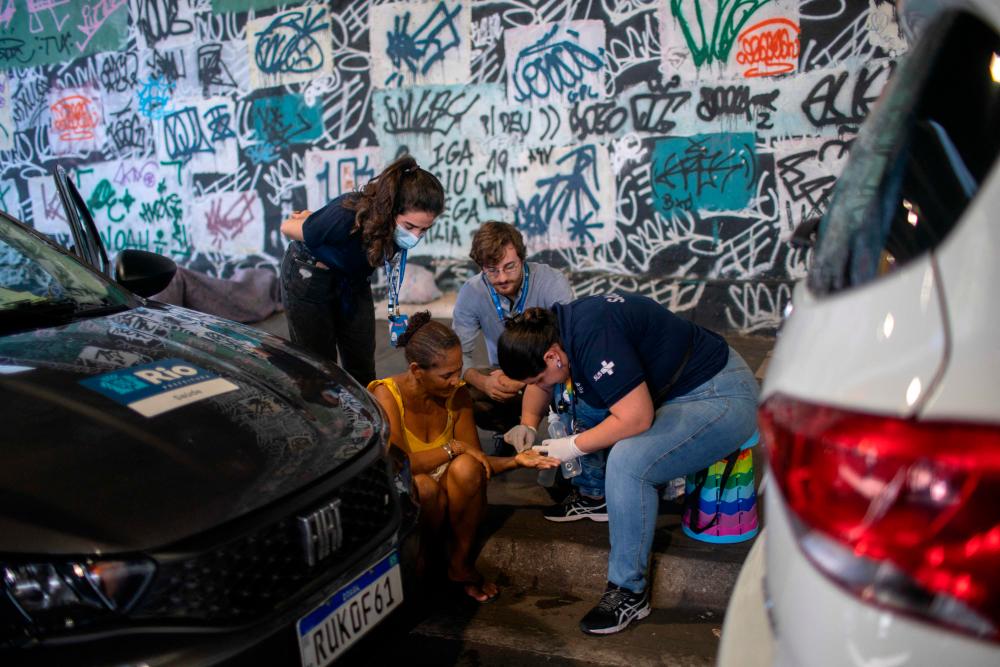 Physician Yasmine Nascimento (R) and medical students provide medical treatment to a homeless woman with her hand injured inside a homeless encampment located under the Madureira viaduct, in north Rio de Janeiro, Brazil on July 31, 2023. AFPPIX