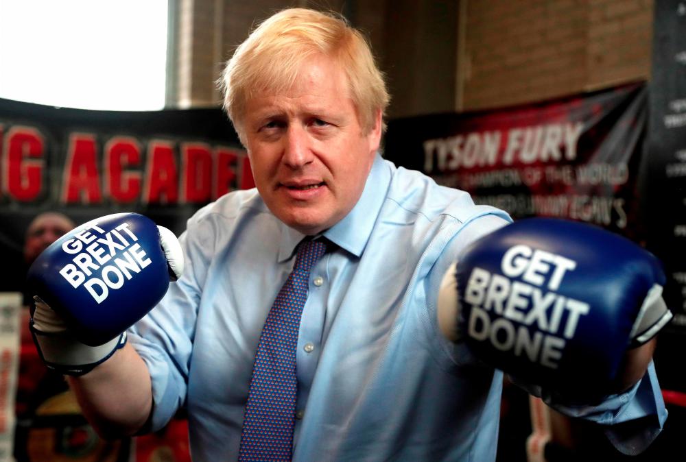Britain's Prime Minister and leader of the Conservative Party, Boris Johnson wears boxing gloves emblazoned with Get Brexit Done as he poses for a photograph at Jimmy Egan's Boxing Academy in Manchester north-west England on Nov 19, during a general election campaign trip. — AFP