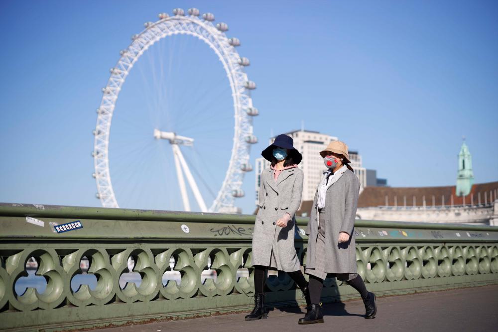 Pedestrians in masks walk along Westminster Bridge with the London Eye in the backgroud, in a quiet central London on March 25, 2020, after Britain's government ordered a lockdown to slow the spread of the novel coronavirus. - AFP