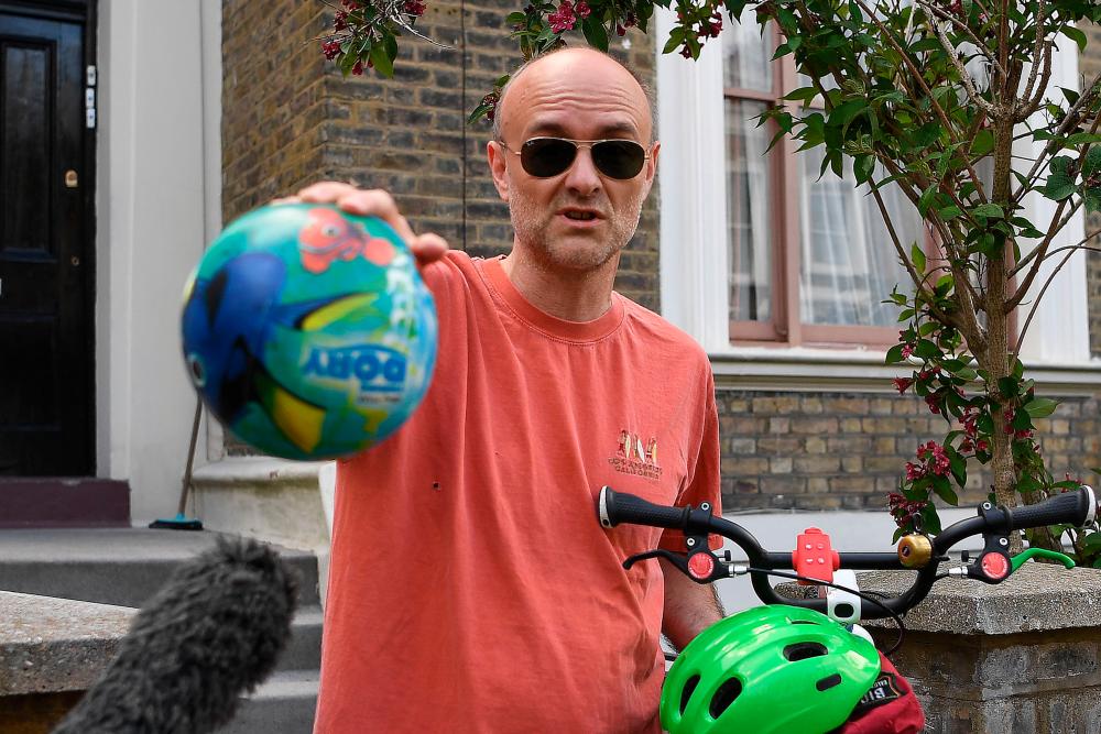Number 10 Downing Street special advisor Dominic Cummings gestures to members of the media to observe social distancing guidelines while he holds a child's bicycle and a ball outside his home in London on May 23, 2020 after allegations he broke coronavirus lockdown rules by travelling across the country in March. The British government on May 23 rejected calls to sack top adviser Dominic Cummings over allegations he broke coronavirus lockdown rules by travelling across the country while displaying symptoms of the disease. Cummings left his London home shortly after he was diagnosed with the virus on March 30, and was later seen with his young son close to his parents' home in Durham, more than 250 miles (400 kilometres) away. / AFP / DANIEL LEAL-OLIVAS