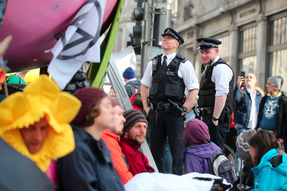 Police officers talk to climate change activists occupying Oxford Circus in the busy shopping district of central London on April 18, 2019 on the fourth day of an environmental protest by the Extinction Rebellion group. — AFP