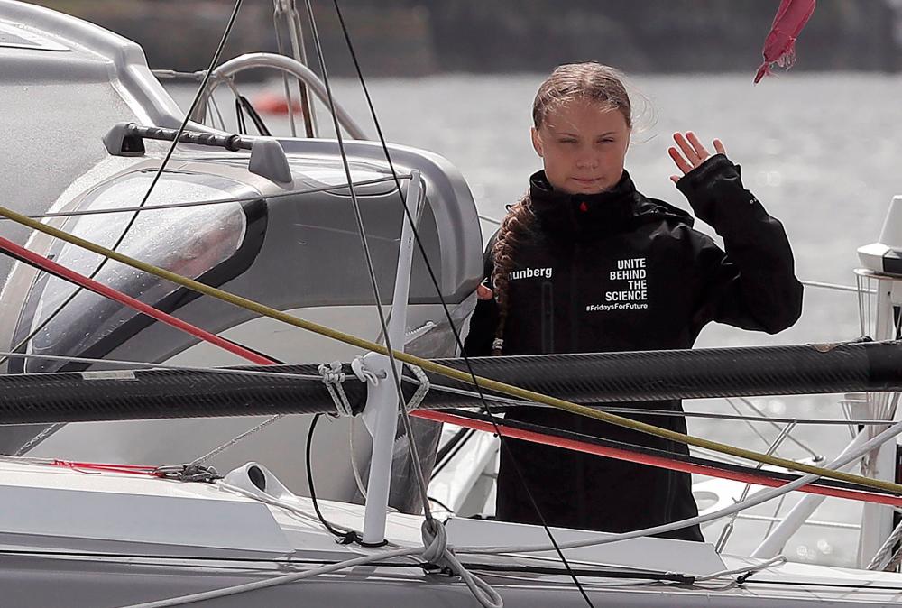 Swedish climate activist Greta Thunberg waves from aboard the Malizia II IMOCA class sailing yacht, off the coast of Plymouth, southwest England, on August 14, 2019, as she prepares to start her journey across the Atlantic to New York where she will attend the UN Climate Action Summit next month. — AFP