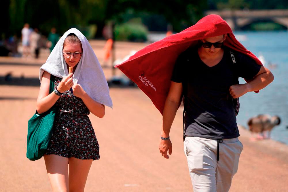 People cover their heads to shelter from the sun as they walk past the Serpentine lake in Hyde Park, west London, on July 19, 2022 as the country experiences an extreme heat wave. AFPPIX