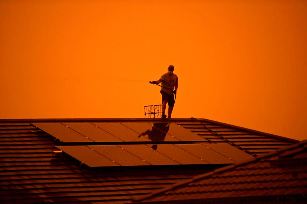 A resident uses a garden hose to wet down the house as high winds push smoke and ash from the Currowan Fire towards Nowra, New South Wales, Australia January 4, 2020. — Reuters