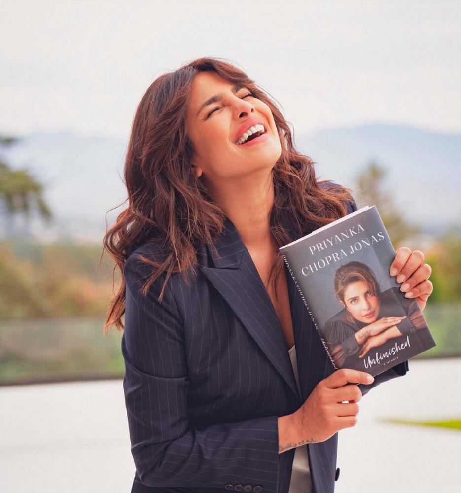Priyanka holding up a copy of her memoir, Unfinished.
