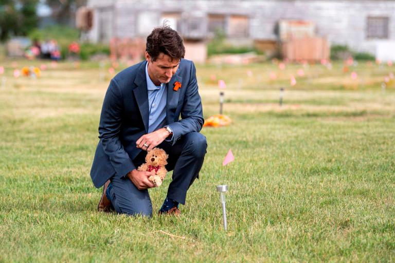 Prime Minister Justin Trudeau lays a teddy bear at a small flag in a field prior to a ceremony at the site of a former residential school on July 6, 2021. — AFP