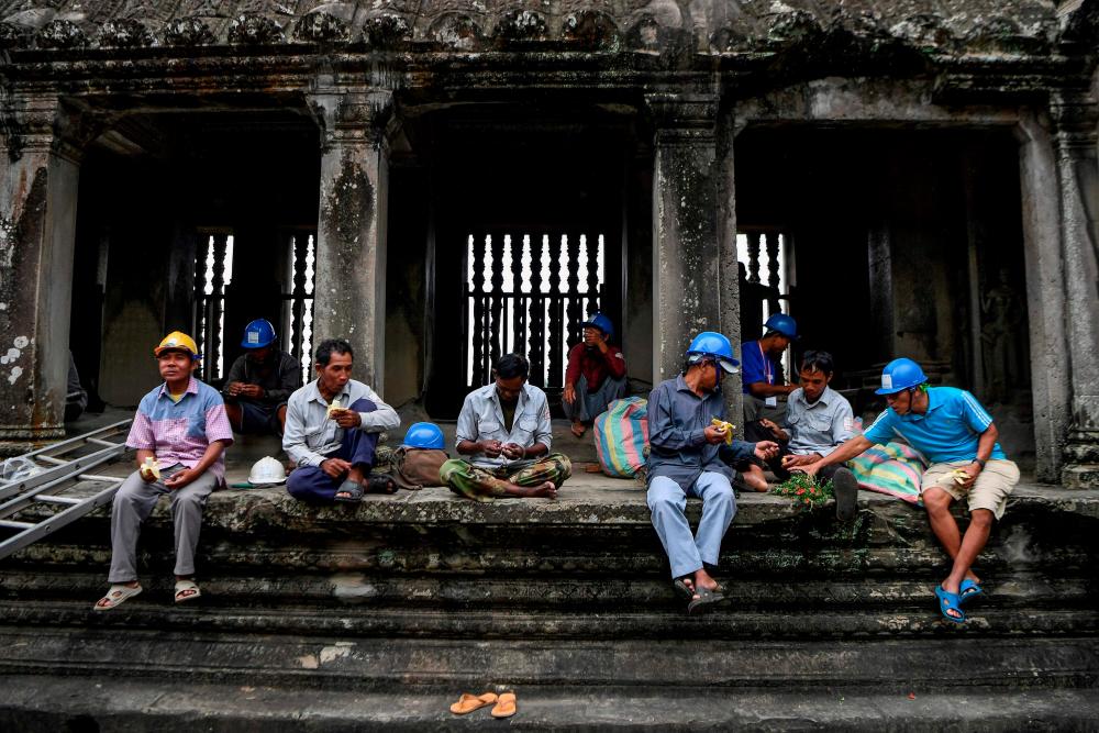 $!This photo taken on October 12, 2020 shows gardeners resting after climbing down from the exterior of the Angkor Wat temple to remove tree saplings in Siem Reap province. AFP / TANG CHHIN Sothy