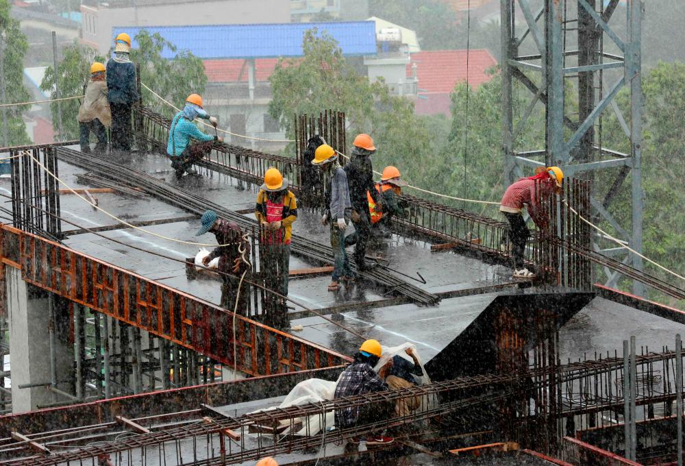Cambodian labourers work under the rain on a high rise building constrtuction site in Sihanoukville. — AFP