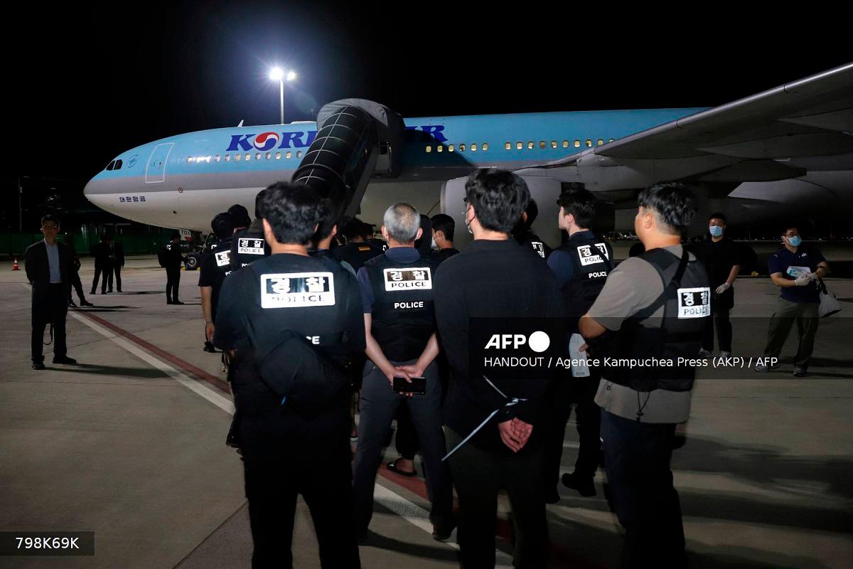 This handout from Agence Kampuchea Press (AKP) taken and released on October 18, 2025 shows South Korean police keeping watch over South Koreans, who had been detained by authorities in Cambodia over alleged cyberscam operations, as they wait to board a chartered plane at Techo International Airport in Kandal province.- AFP PHOTO / AGENCE KAMPUCHEA PRESS (AKP)