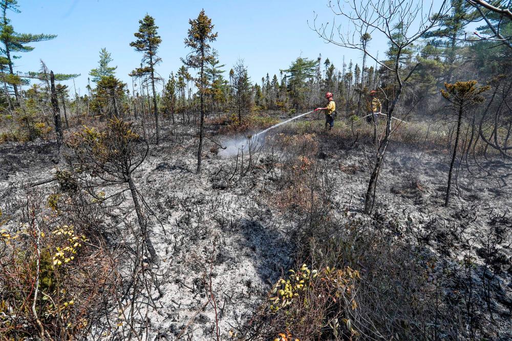 This June 1, 2023, image courtesy of the Nova Scotia Government in Canada, shows firefighters Walter Scott and Zac Simpson spray the ground around Barrington Lake, Shelburne county, Canada/AFPPix