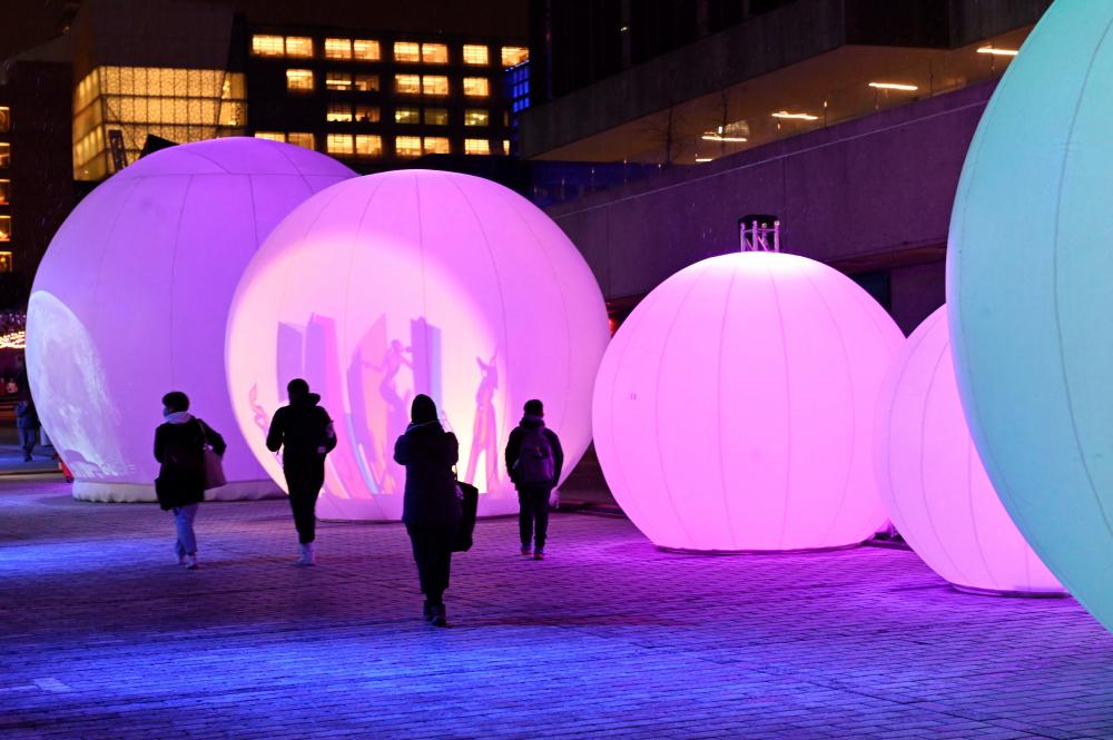 $!People enjoy the ‘New Moon’ sound-and-light installation, consisting of seven inflated spheres that reveal through shadows and light, iconic images and stories inspired by the culture of the Quartier des Spectacles, on December 14, 2020 in Montreal, Quebec, one of the five light installations on display to bring some comfort to residents of a city that has been battered by months of coronavirus. AFP / Eric THOMAS