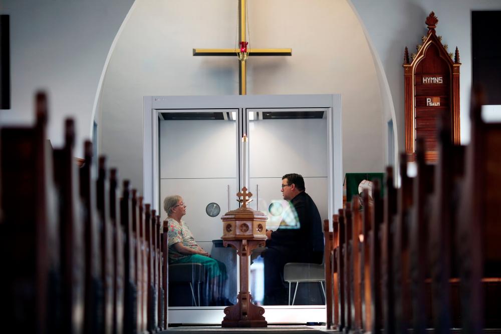 Pastor Rev. Joel Crouse (R) of Saint John Lutheran Church chats with a parishioner in a see-through, 4’ x 6’ enclosed compartment, called the “God Pod” on Sept 16, 2020 in Ottawa, Canada. — AFP