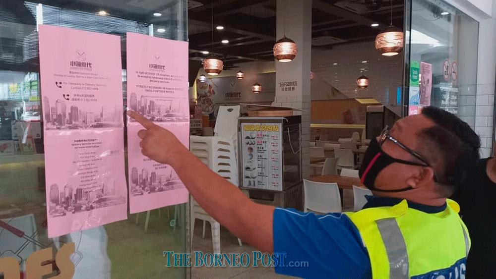 $!A policeman points to a sign that says only take-aways are allowed when conducting inspections at a commercial centre in Kuching to enforce the Movement Control Order which came into force on March 18. — The Borneo Post