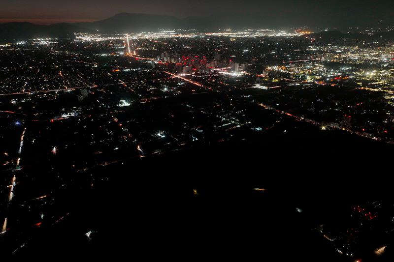 This aerial view shows the city partially illuminated during a blackout in Santiago on February 25, 2025. In the middle of the austral summer season, Chile is facing this Tuesday an unusual and massive blackout due to an alleged failure of the power system, which forced the evacuation of the Santiago subway and plunged the population into confusion. - Javier TORRES / AFP