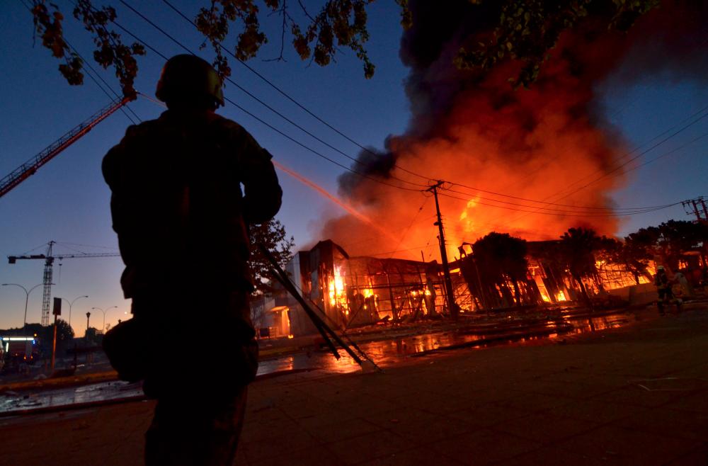 A soldier looks on as firefighters combat a fire destroying a supermarket in Concepcion, Chile, on the fourth straight day of protests against a now suspended hike in metro ticket prices, on Oct 21, 2019. — AFP