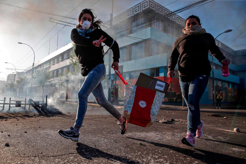 A looter flashes the V sign as she runs during protests in Valparaiso, Chile, on Oct 20, 2019. — AFP