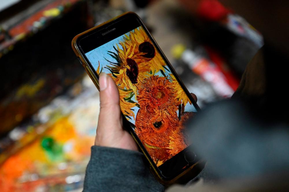 This picture taken on February 19, 2023 shows artist Deng Fei using an image on his phone for reference as he paints a replica of Vincent van Gogh’s Sunflowers in an alley at Dafen village, in Shenzhen, in China’s southern Guangdong province. AFPPIX