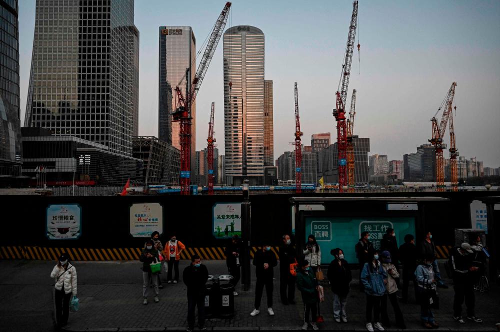 Commuters waiting at a bus stop near a construction site at central business district in Beijing. China has lent hundreds of billions of dollars to build infrastructure in developing countries. – AFPpic