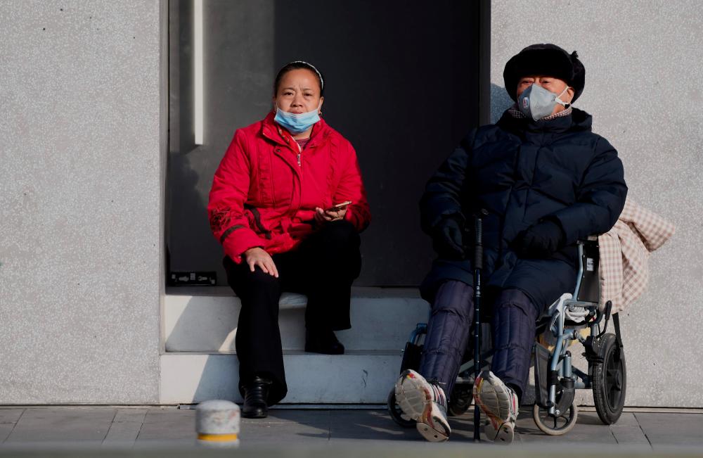People wearing protective masks relax in the sun along a street in Beijing on Jan 24. — AFP