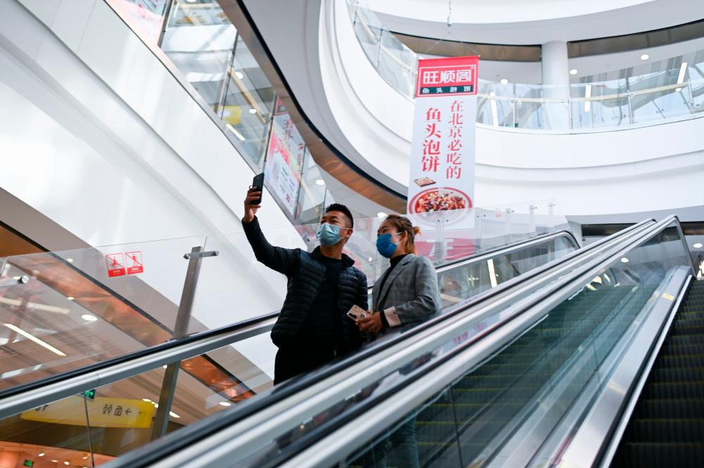 A man and a woman wearing face masks use a mobile phone to take a selfie in a mall in Beijing on April 2, 2020. - AFP