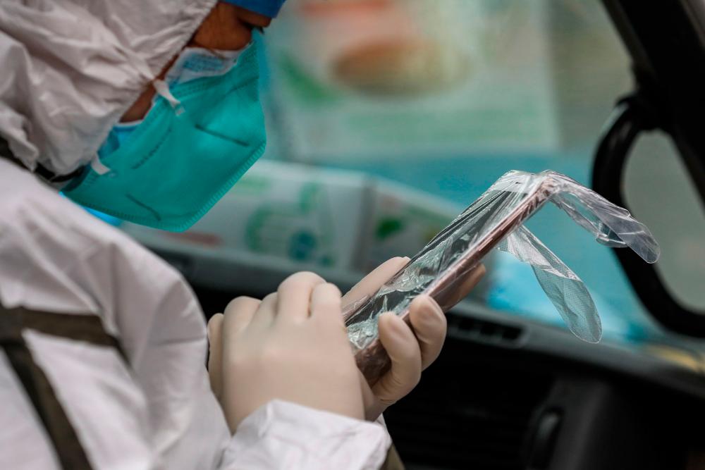This photo taken on January 26, 2020 shows a medical staff member wearing protective clothing to help stop the spread of a deadly virus which began in the city, using her smartphone covered in a plastic disposable glove, on an ambulance as she organises transferring patients, in Wuhan in China's central Hubei province. - AFP