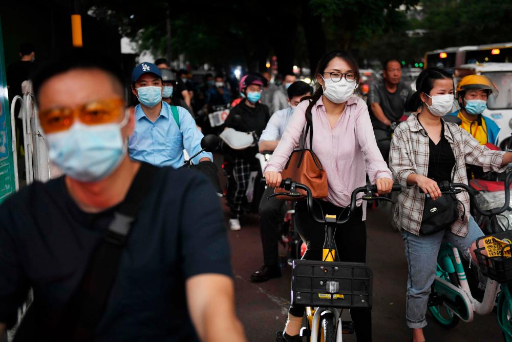 People wearing face masks wait to cross a busy interesection in Beijing on June 1, 2020. — AFP