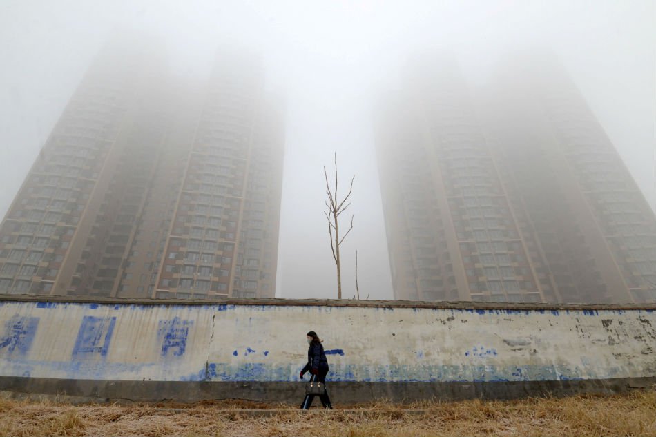 A woman wearing a mask walks past buildings on a polluted day in Handan, Hebei province, China — Reuters