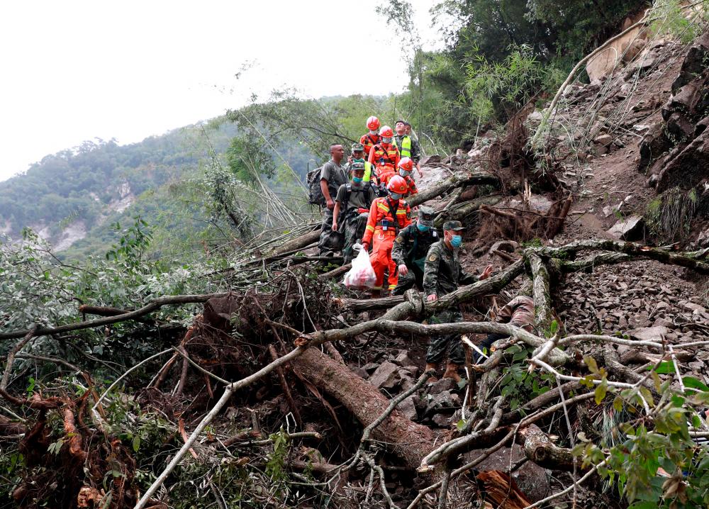 This photo taken on September 6, 2022 shows rescuers walking past uprooted trees from a landslide as they head to an earthquake-affected area following a 6.6-magnitude earthquake that struck September 5, in Shimian county, Ya’an city/AFPPix