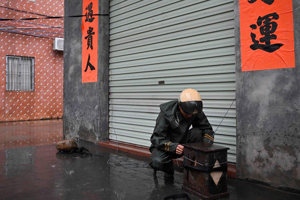 A man ties down the shutters of his premises onto a weight during the passing of Super Typhoon Ragasa in Yangjiang, southern China’s Guangdong province on September 24, 2025. - ADEK BERRY / AFP