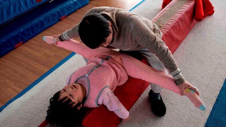 In this picture taken on January 11, 2021, coach and deputy headmaster Liu Fen (right) helps a young gymnast stretch her legs at the Li Xiaoshuang Gymnastics School in Xiantao, Hubei province. – AFPPIX
