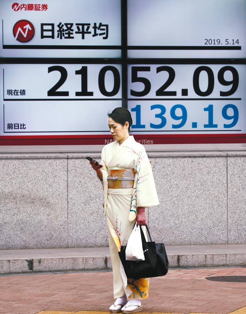 File picture of a woman in front of an electronic board showing the Nikkei index outside a brokerage in Tokyo. The Nikkei 225 posted its second biggest slide so far this year. – REUTERSPIX