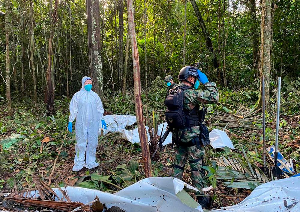 Forensic scientist (L) and soldiers standing next to the wreckage of an aircraft that crashed in the Colombian Amazon forest in the municipality of Solano, department of Caqueta, on May 19, 2023.
