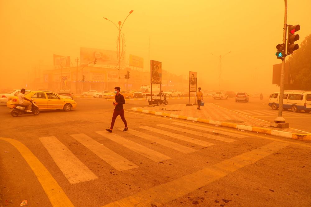 A pedestrian crosses a road in the city of Nasiriyah in Iraq’s southern Dhi Qar province on May 16, 2022 amidst a heavy dust storm. AFPPIX