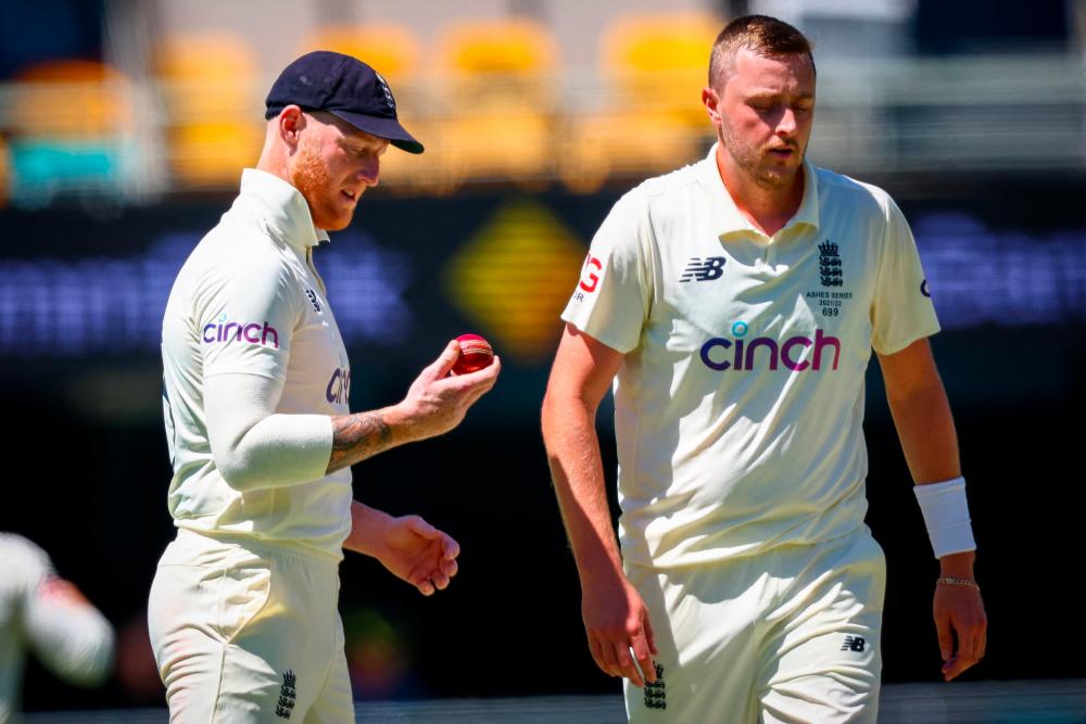 England's Ben Stokes (L) shines the ball as teammate Ollie Robinson (R) returns to his mark during day two of the first Ashes cricket Test match between England and Australia at the Gabba in Brisbane on December 9, 2021. AFPpix
