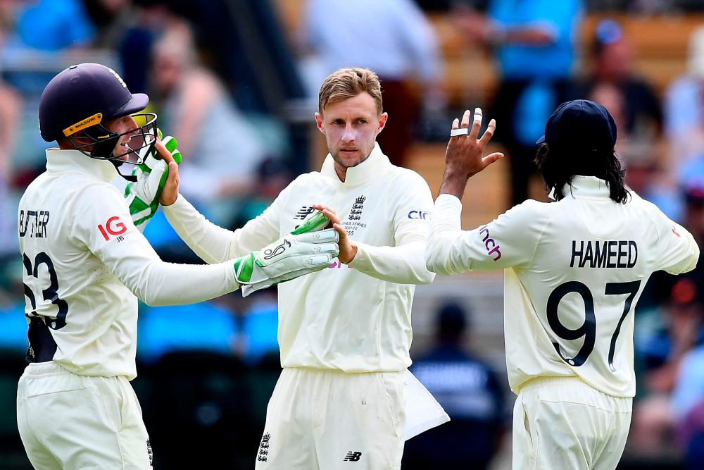 England's Joe Root (C) celebrates the wicket of Australia's Batsman Travis Head (not pictured) with teammates Jos Buttler (L) and Haseeb Hameed on day two of the second cricket Test match of the Ashes series at Adelaide Oval on December 17, 2021, in Adelaide. AFPPIX