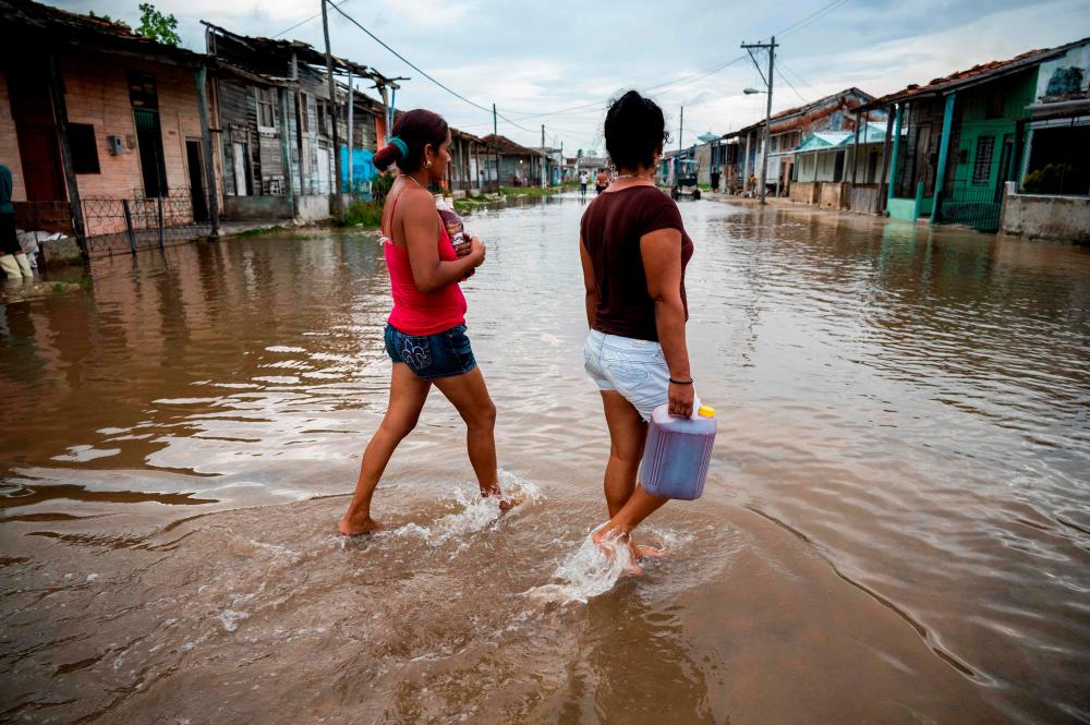 Women walk in a flooded area of Batabano, Mayabeque Province, Cuba, on August 28, 2023, as Tropical Storm Idalia approaches the western tip of the island nation. AFPPIX
