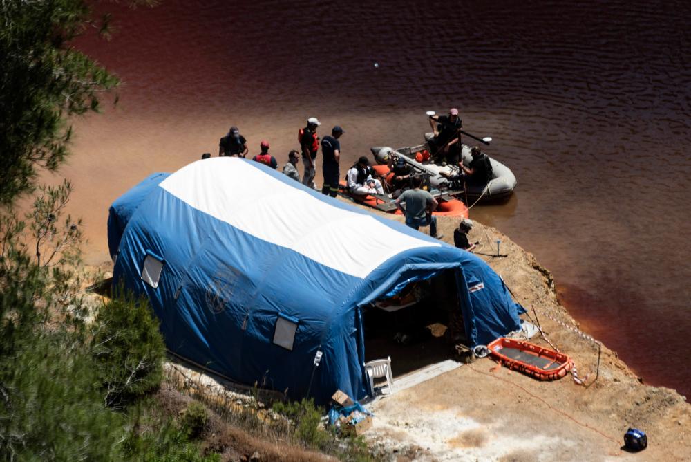 Forensic police officers and investigators gather near a boat equipped with a sonar system before it sails on the acidic Red Lake near the village of Mitsero, southwest of the capital Nicosia, during the search for possible bodies of victims of a suspected serial killer, on May 4, 2019. — AFP