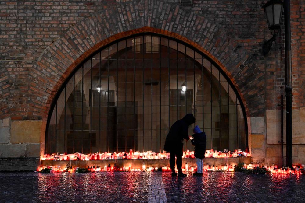 A mother and her child place a candle at a makeshift memorial for the the victims of the Charles University's shooting, outside the Charles University in central Prague, on December 23, 2023, during a national mourning day. - AFPPIX