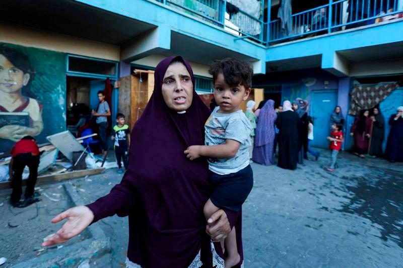 A Palestinian woman carrying a child reacts after an Israeli air strike on a school sheltering displaced people in al-Nuseirat on Saturday - REUTERSpix