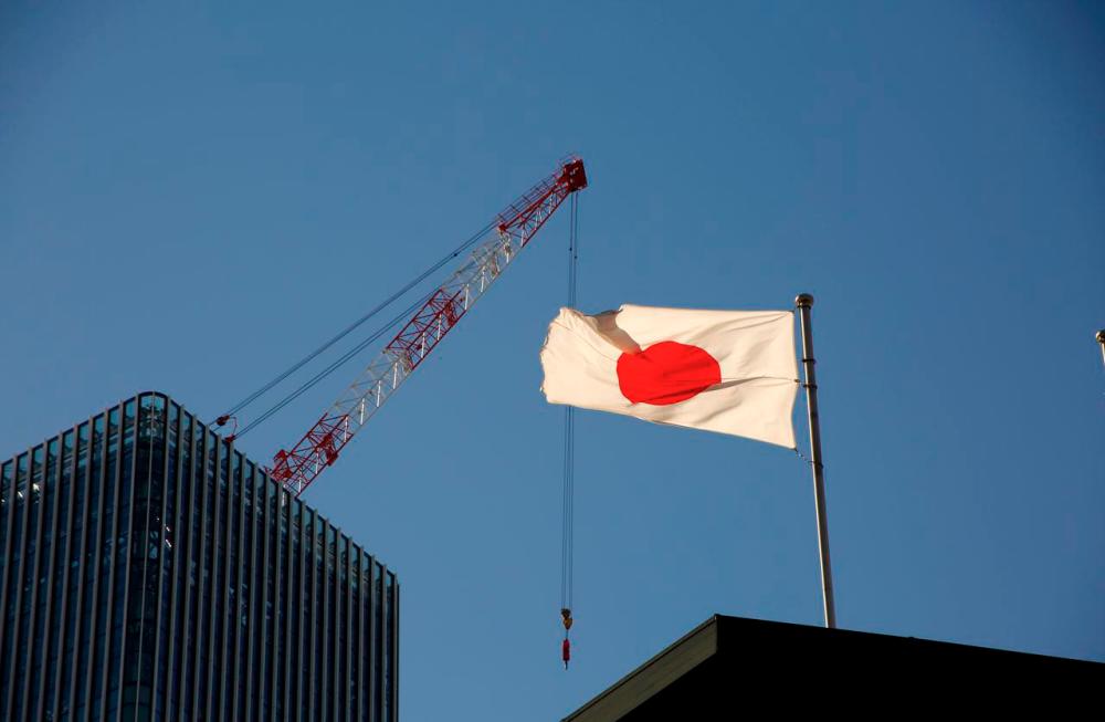 Japan’s national flag is seen in front of a crane at a construction site at a business district in Tokyo, Japan