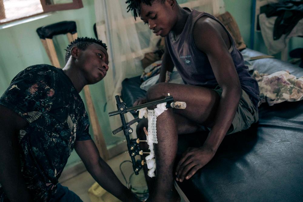 A young man with a gunshot wound to the leg asks a friend for help at Rutshuru Hospital in the eastern province of North Kivu, Democratic Republic of Congo, on July 23, 2022. - AFPPIX
