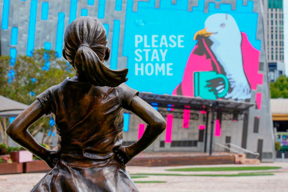 The Fearless Girl Statue looks at a “Please Stay Home” sign in an empty Federation Square...-Reuters