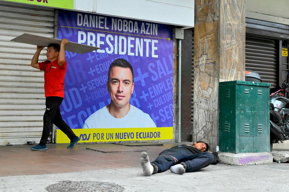 A man sleeps in the street while another person walks in front of advertisement for Ecuador's presidential candidate of the National Democratic Action Party, Daniel Noboa, in Guayaquil, Ecuador, on October 13, 2023. AFPPIX