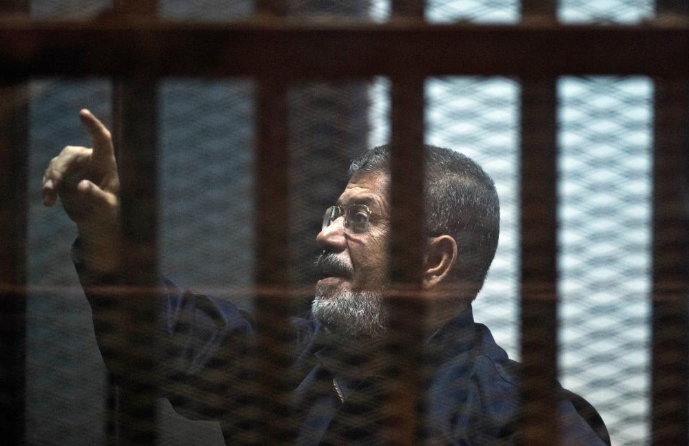 Egypt's ousted Islamist president Mohamed Morsi stands behind the bars during his trial in Cairo on June 16, 2015. — AFP