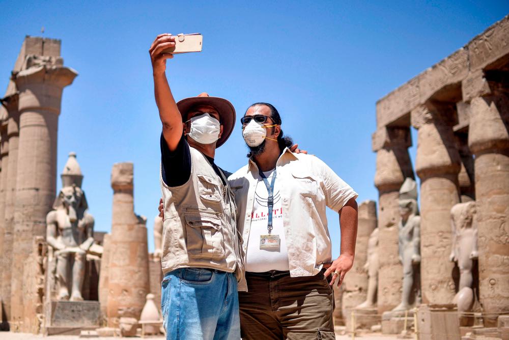 Mask-clad tour guides pose together for a “selfie” on a cell phone at the colonnade of the ancient Temple of Luxor in Egypt’s southern city of Luxor on July 1, 2020, as the country eases restrictions put in place due to the COVID-19 coronavirus pandemic. / AFP / -