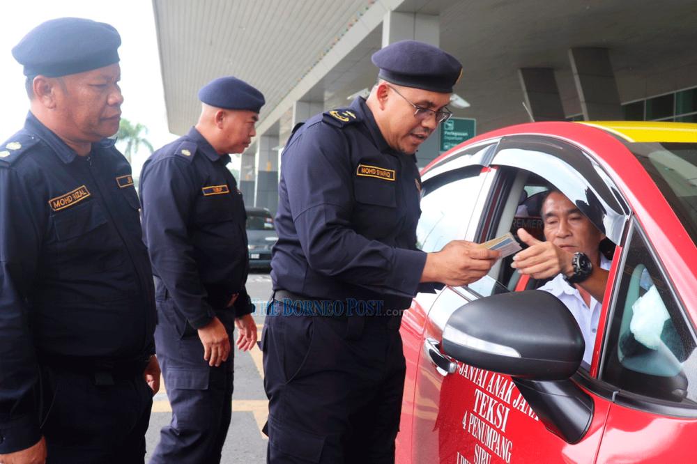 Mohd Syafiq checks the licences of a taxi driver, who is also an e-hailing driver the operation at Sibu Airport. — TheBorneoPost
