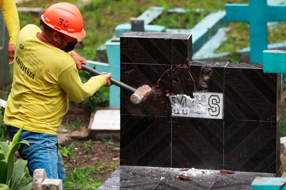 This handout picture released by El Salvador’s Presidency shows an inmate destroying a grave with symbology alluding to the Mara Salvatrucha (MS-13) gang at a cemetery in Santa Tecla, El Salvador, on November 3, 2022. AFPPIX