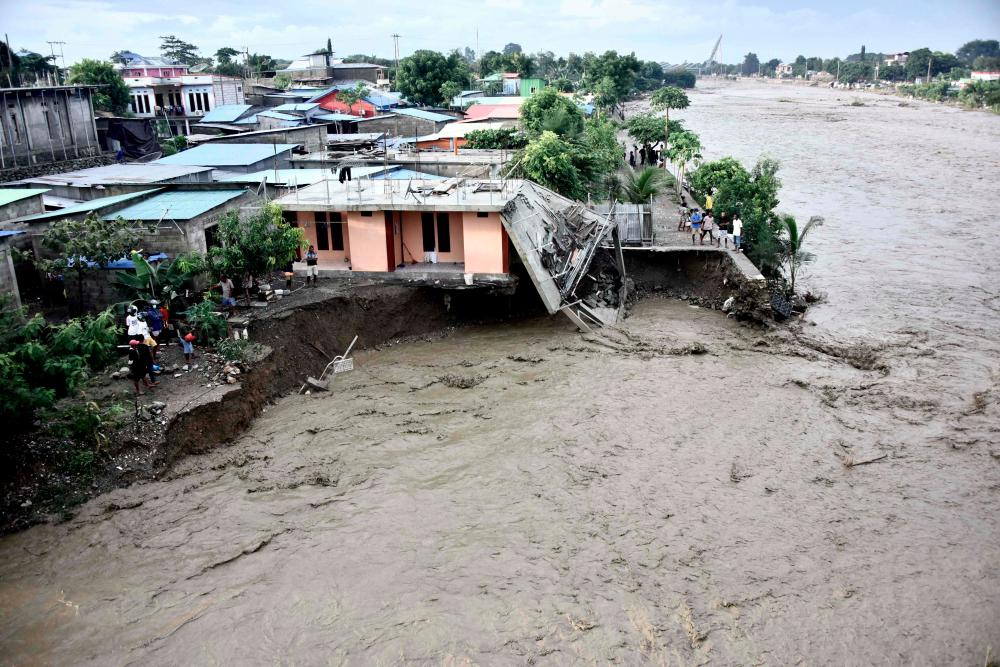 Residents stand along the water’s edge by damaged homes after heavy rains and strong winds lashed East Timor’s capital Dili overnight causing extensive flooding on April 4, 2021. - AFP